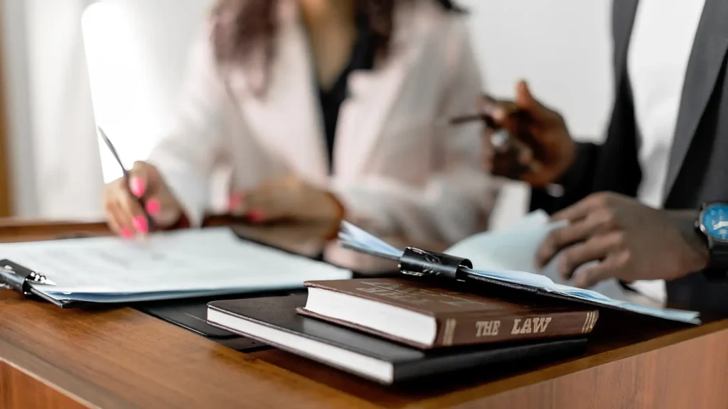 Law books on a desk with two professionals discussing in the background.