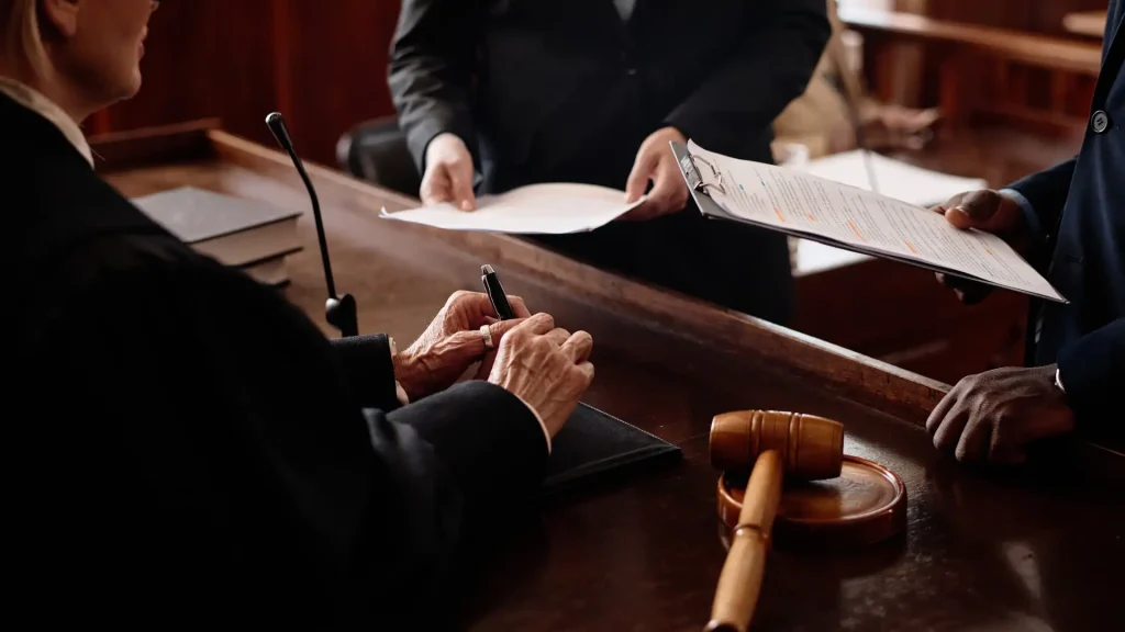 Judge signing documents with a gavel on the desk in a courtroom.