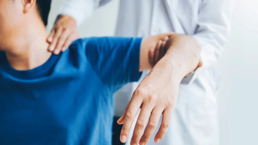 A person receiving physical therapy, with a therapist adjusting their arm in a clinical setting.
